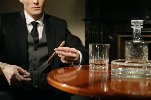 a man in a suit at a table with a drink and cigar