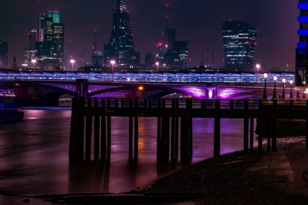 a bridge over the river Thames in London lit up in purple lights at night