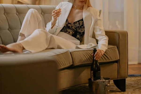 an older lady laying on a sofa drinking champagne in a white suit