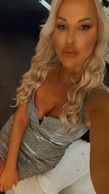 Blonde escort Ana is wearing a low cut silver dress 