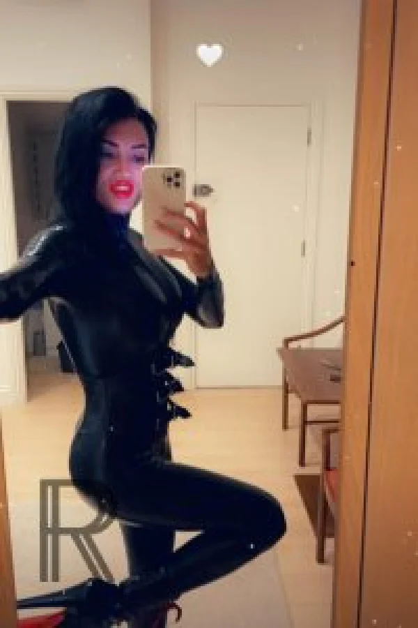 Mistress Elizabeth taking a selfie wearing a latex bodysuit