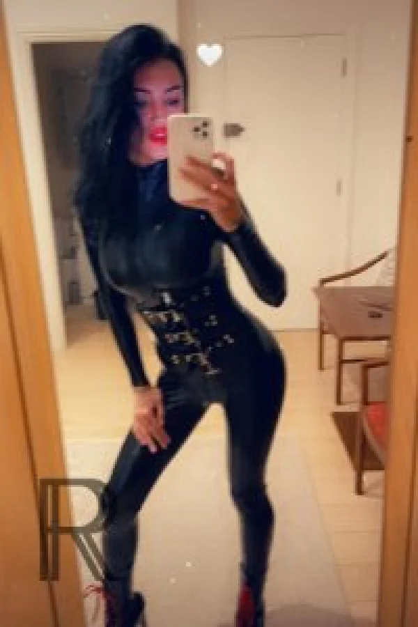 Mistress Elizabeth taking a selfie wearing a latex bodysuit