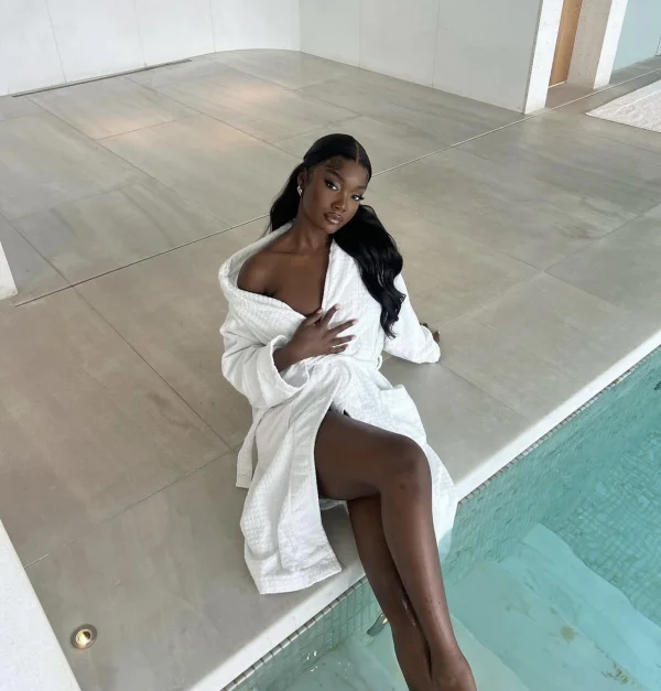 Elam is sitting on the side of a swimming pool wearing just a robe 