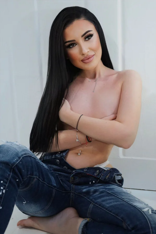 A sexy brunette London escort who is topless with her arms folded across her chest 