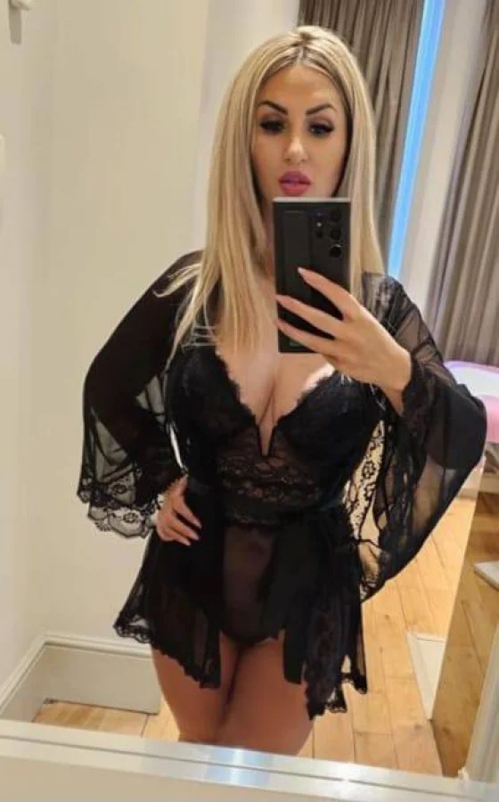A good looking blonde escort is wearing a sexy black basque 