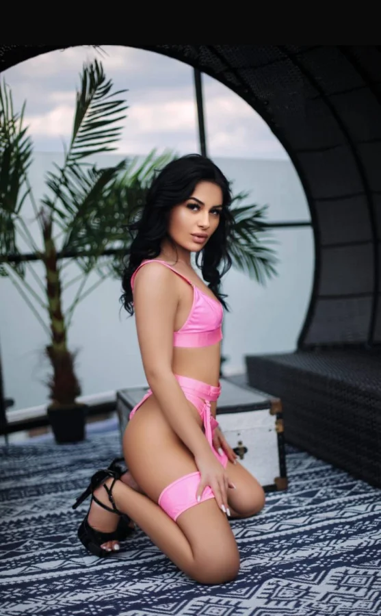 Slim brunette escort Ella-Jane is kneeling down on the floor and looking at the camera 
