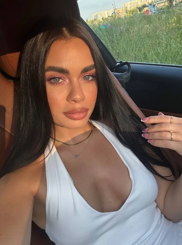 Brunette escort Blossom wearing a low cut white dress 