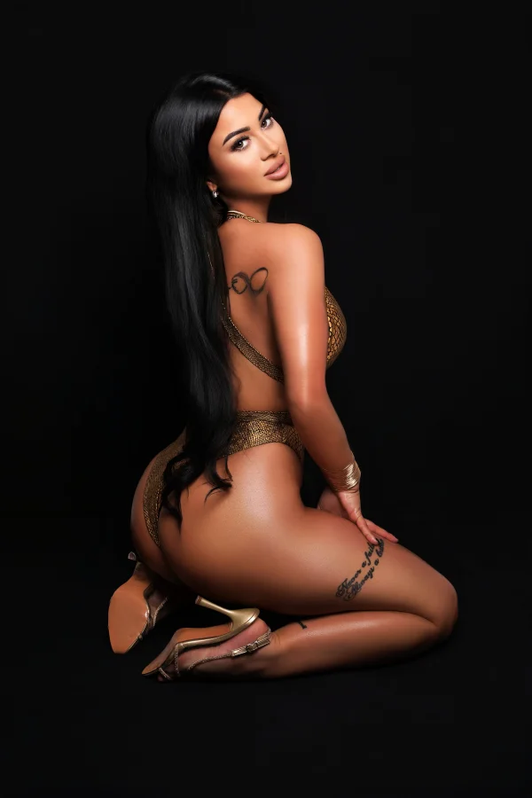 Gorgeous Eastern European escort in gold swimsuit, kneeling seductively