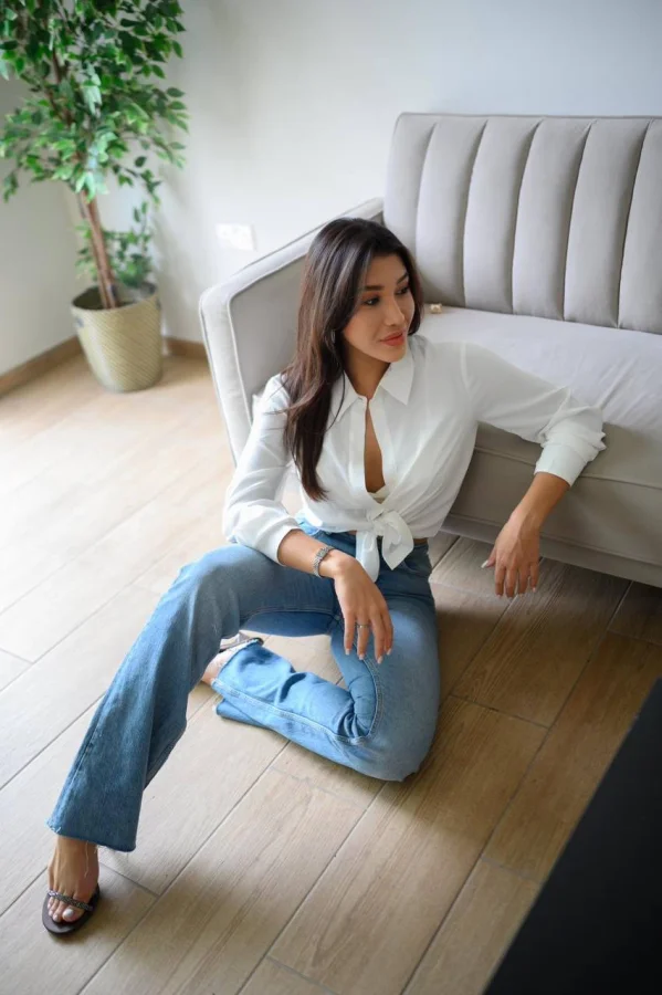 A lady sitting on the floor wearing jeans and a white shirt 