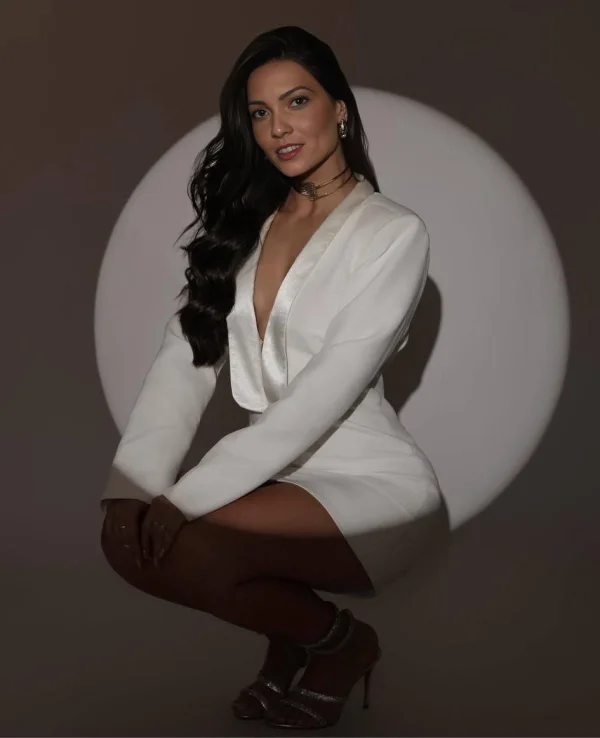 Raya is wearing a low cut white dress that shows off her figure 