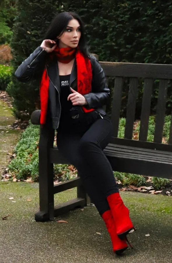 Brunette woman wearing black and red sitting on a park bench 