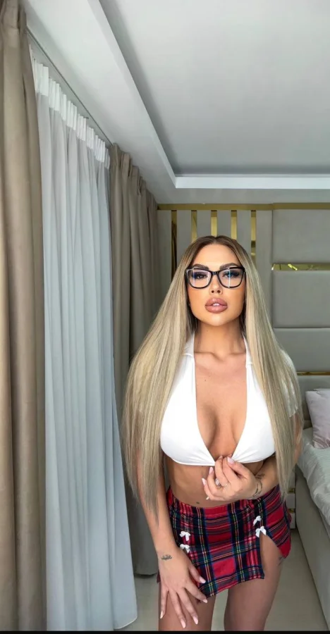A busty blonde escort wearing a very low cut white top 