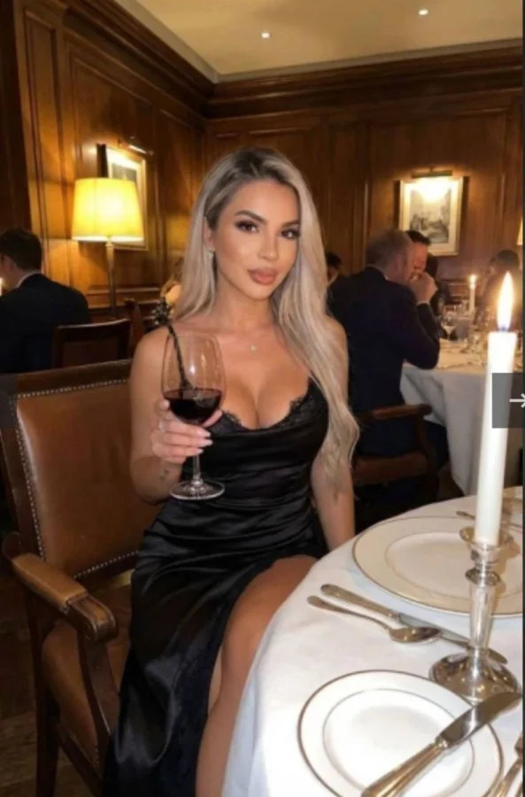 A very sexy lady wearing a black dress enjoying as glass of wine 